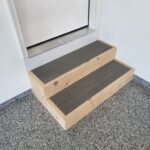 Two-rise exterior steps with closed risers, natural wood sides, dark treads, installed at door threshold.