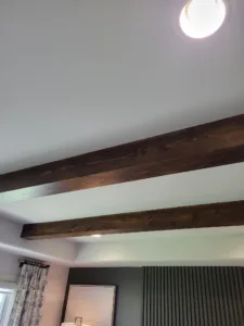 Dark stained wood beam on a sloped bedroom ceiling near a round light fixture