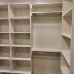 Finished face-frame closet system with painted white shelving, hanging rods, and cubby storage in walk-in closet.
