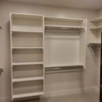 Finished walk-in closet with white face-frame shelving, multiple hanging rods, and tiered shelf storage.