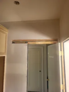 Unpainted wood backer board and barn door track mounted above a doorway, ready for the door slab