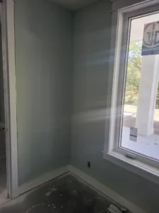 Painted room corner with finished white casing framing a window, bright daylight through the glass.