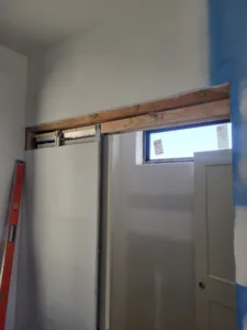 Wood header and barn door track blocking installed above a window, plastic sheeting protecting walls