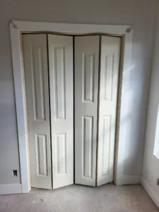 Cream painted bifold closet doors closed, natural wood casing left unfinished