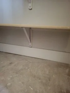 Unfinished wood cap board mounted on wall brackets, with unpainted drywall and a bare subfloor below
