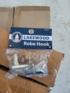Metal robe hook still sealed in its packaging with mounting hardware visible, before installation.