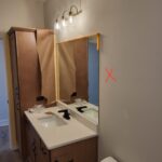 Finished bathroom vanity with wood cabinets, white countertop, framed mirror, and pendant lighting installed.