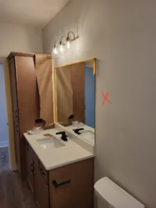 Bathroom vanity with wood cabinets, white countertop, mirror, and a wall mounted light bar