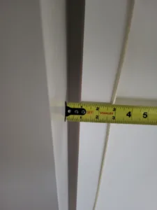 Tape measure held against a painted mitered trim edge during a fit check.