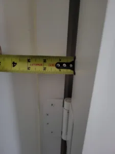 Tape measure held against a painted door edge above a hinge during installation