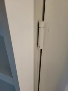 Painted white door edge with a small pivot hinge mounted flush against the jamb
