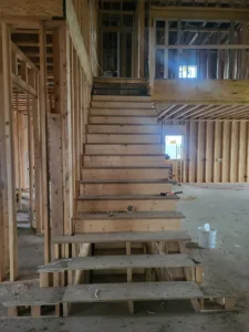 Long open riser staircase framed within unfinished house construction, raw lumber treads and studs visible.
