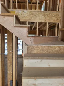 Stair stringer framing with OSB tread substrate and exposed studs, rough construction before finish work.
