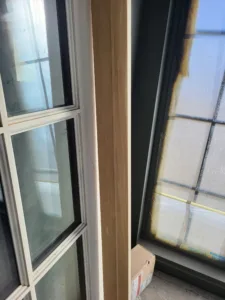 Unfinished wood mullion strip installed vertically between two adjoining multi-lite windows.