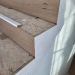 Wood nosing installed on stair tread edges with primed riser boards—raw wood treads ready for finish.
