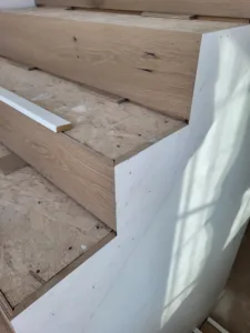 Wood nosing installed on stair tread edge over OSB subfloor, primed trim piece visible nearby