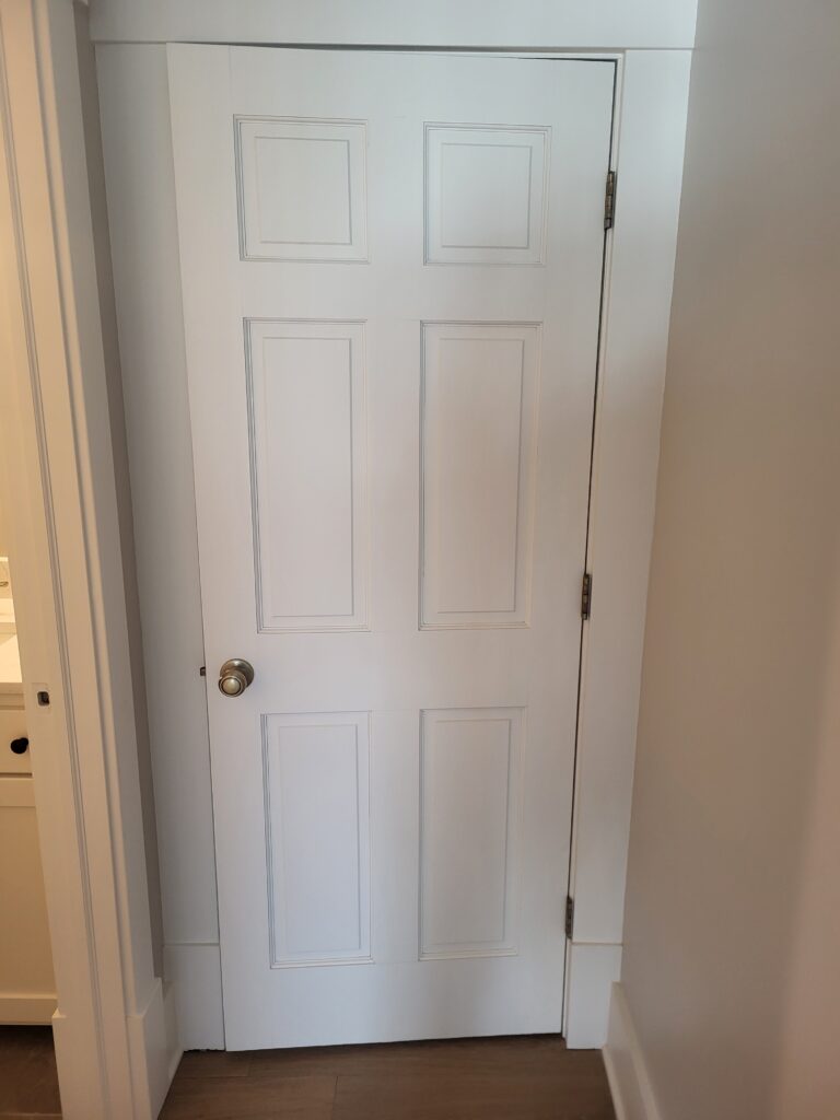 White six-panel interior door with casing and black hinges.