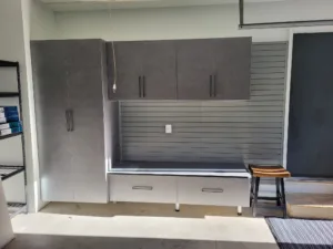 Garage cabinet wall with gray upper cabinets, center slatwall panel, and lower storage bench, complete.