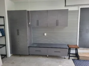 Garage cabinet wall with gray upper cabinets, slatwall panel, and lower bench with drawers, installed.