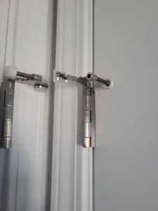 Chrome hinge and pivot guide hardware installed on the edges of white bifold closet door panels.