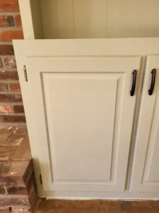 White cabinet doors with recessed panel detail and black bar pulls installed, brick wall behind