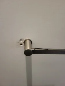 Round bronze rod bracket mounted on a painted wall with mounting screws visible