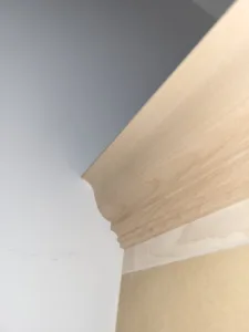 Unfinished natural wood crown molding installed at wall corner, raw profile ready for paint or stain.