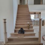 Completed wood staircase with finished treads, risers, newel posts, and handrail in raw wood before painting.