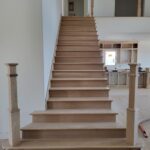 Completed stair assembly with finished treads, risers, newel posts, and handrail—raw wood ready for stain or paint.