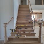 Finished stair assembly with wood treads, risers, newel posts, and handrails installed—raw wood ready for paint.