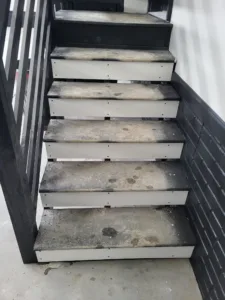Garage steps with closed risers, black metal railing and white riser boards, treads worn and dirty.