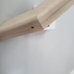 Close-up of a wood wall cap installation showing the joinery and mounting details. The wood is unfinished and highlights craftsmanship.
