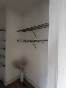 Corner-mounted wire closet shelf and rod installed diagonally, wood laminate flooring below.