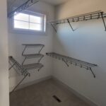 Wire shelving and hanging rods installed in closet with painted walls and window.