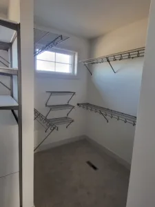 White wire shelving and hanging rods installed in closet with a window on the back wall.