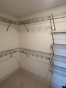 White wire shelving and hanging rods installed at inside corner of closet, painted walls and ceiling.