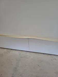 Primed white baseboard installed at the wall to floor junction, top edge uncaulked, ready for paint.