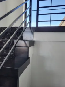 Dark stained wood stair tread end caps beside a black metal horizontal bar railing