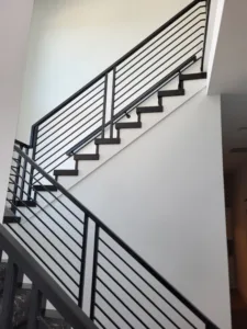 Modern staircase with horizontal black metal rod railing between wood posts and painted skirt board