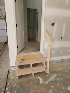 Garage stair with two open treads (three risers) up to a house door, raw wood, handrail post at right