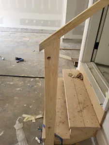 Raw wood handrail post and small step platform framed near an exterior door opening.