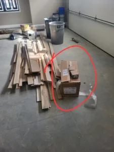 Trim boards and a hardware box staged on a garage floor before cabinet installation.