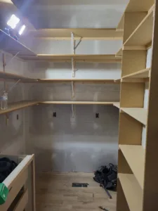 Closet with several raw wood particle board shelves installed at graduated heights, unpainted.