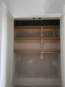 Closet interior with three raw wood shelves and cleats installed, unpainted framing stage.