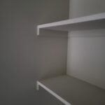 Two white-painted closet shelves with support brackets installed in raw drywall opening.