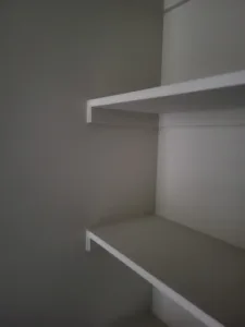 Two painted white closet shelves with support brackets mounted in a corner nook, gray wall.