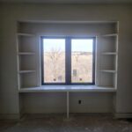 Custom built-in bookcase with open shelving on both sides of window, raw wood and drywall ready for paint.