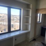 Raw wood window seat with countertop and open shelving above, unpainted finish.