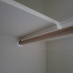 Closet hanging rod with wood-grain finish and white mounting bracket installed between walls.