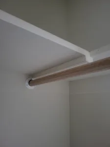 Closet hanging rod detail with a wood grain finish and a white mounting bracket between walls